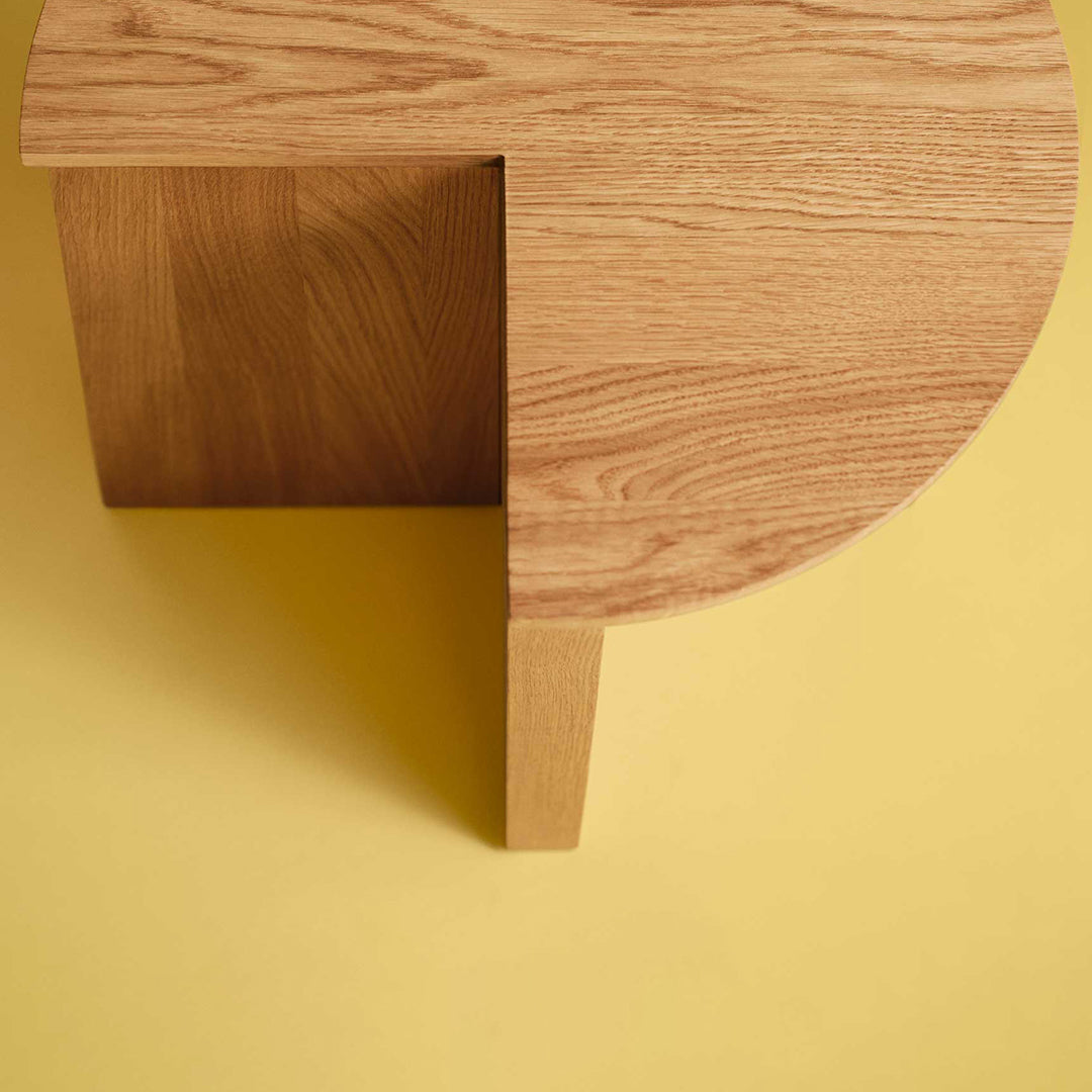 Wooden coffee table with a circular top and contrasting square base on a yellow background. Natural oak finish.