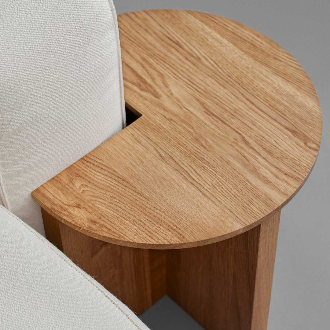 Light wood grain side table with a circular top, complemented by a soft white upholstery. Modern and minimalistic design.