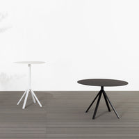 Two modern round tables: one sleek white and one elegant black, featuring geometric tripod legs against a neutral backdrop.