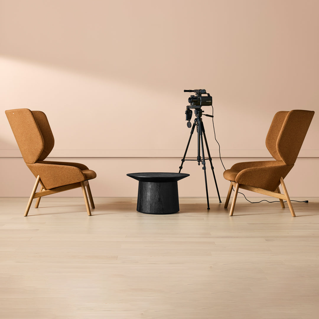 "Stylish tan armchairs with sleek black accent table on light wood floor against soft pink wall backdrop."