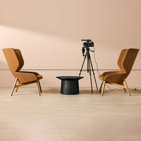 "Stylish tan armchairs with sleek black accent table on light wood floor against soft pink wall backdrop."