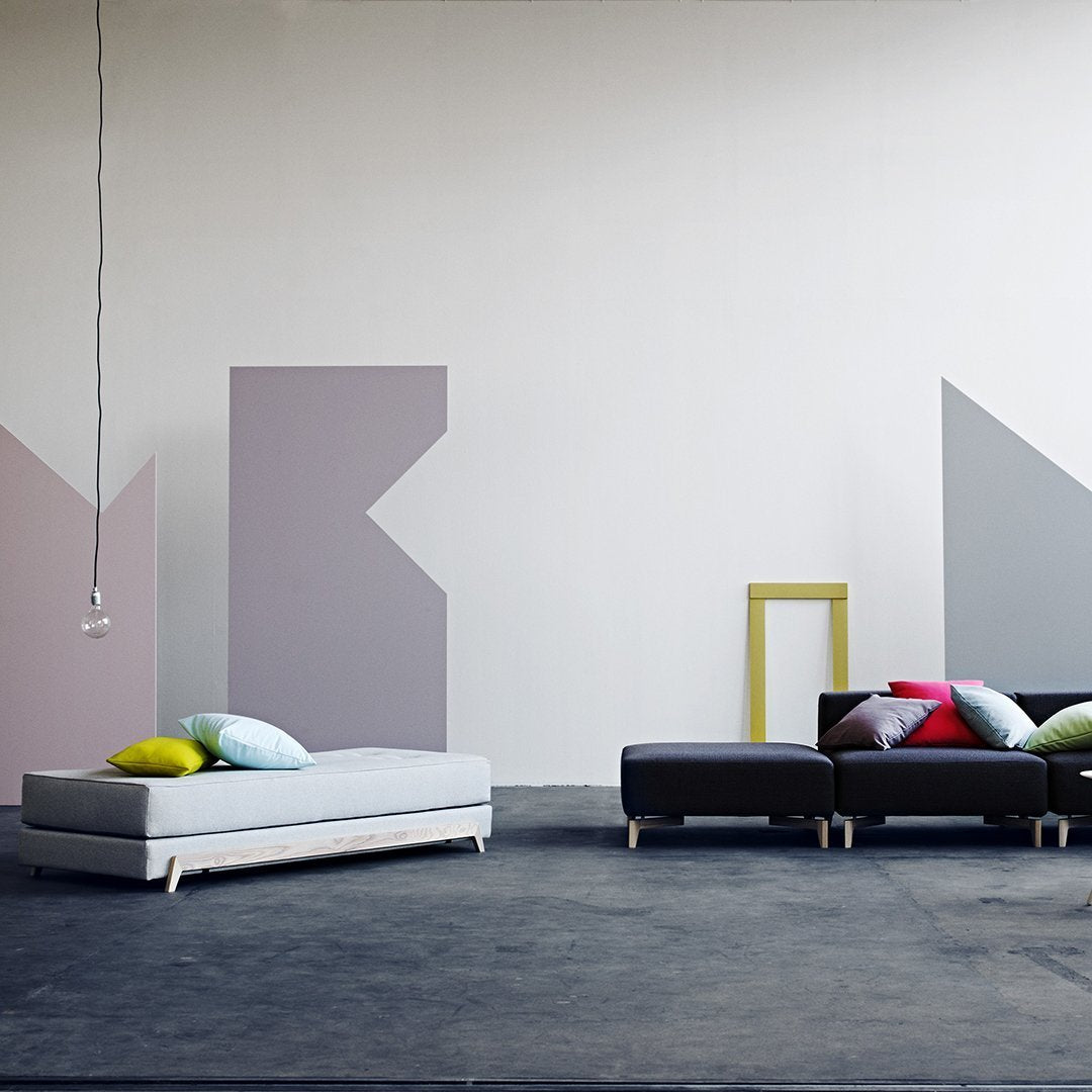 Contemporary furniture set featuring gray, black, and colorful pillows against abstract pastel wall patterns.
