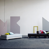 Contemporary furniture set featuring gray, black, and colorful pillows against abstract pastel wall patterns.