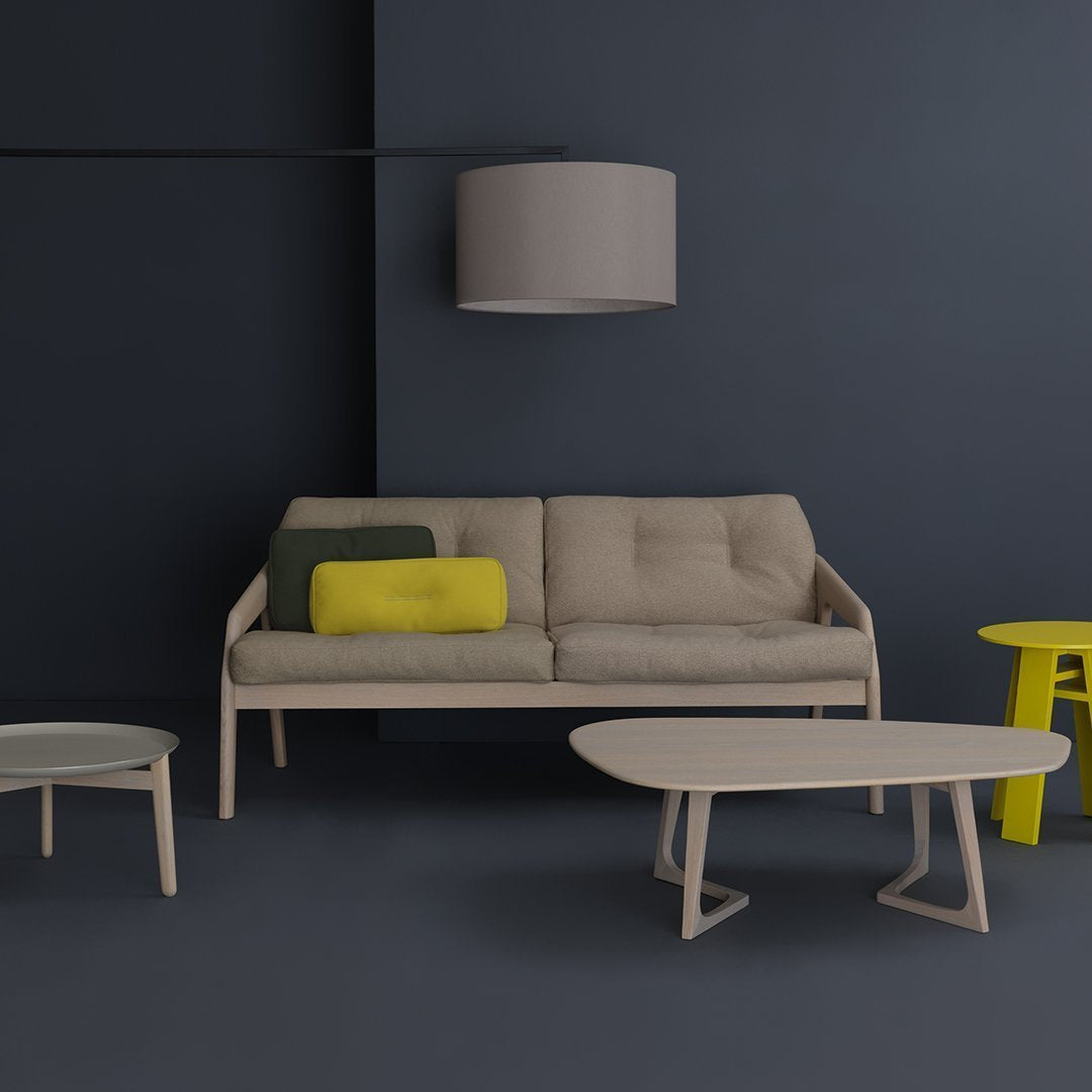 Beige sofa with yellow and green pillows, round and oval beige tables, set against a dark blue wall.