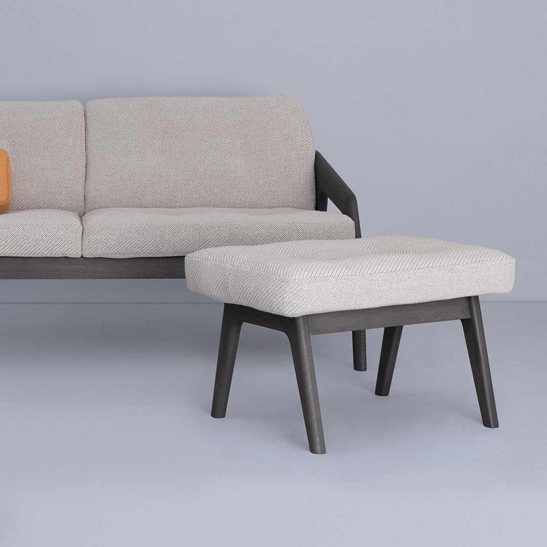 Light gray textured fabric ottoman on dark wood legs, complementing a light gray sofa against a soft blue background.