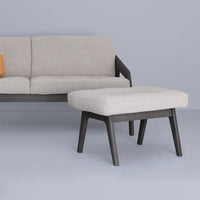 Light gray textured fabric ottoman on dark wood legs, complementing a light gray sofa against a soft blue background.
