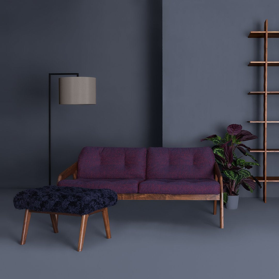 Purple sofa with button detailing, complemented by a dark patterned ottoman against a gray background.