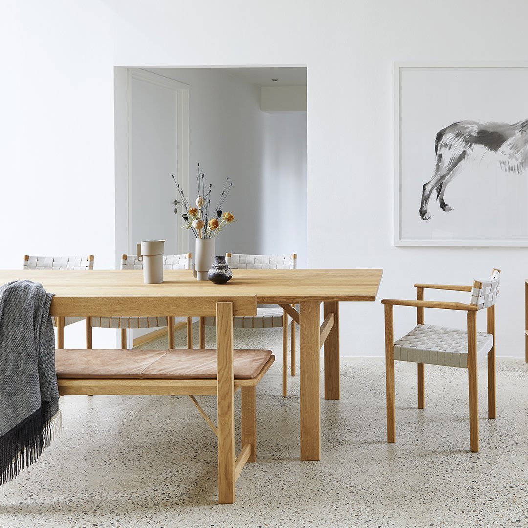 Light wood dining table with neutral gray and beige patterned chairs in a minimalist, modern setting.