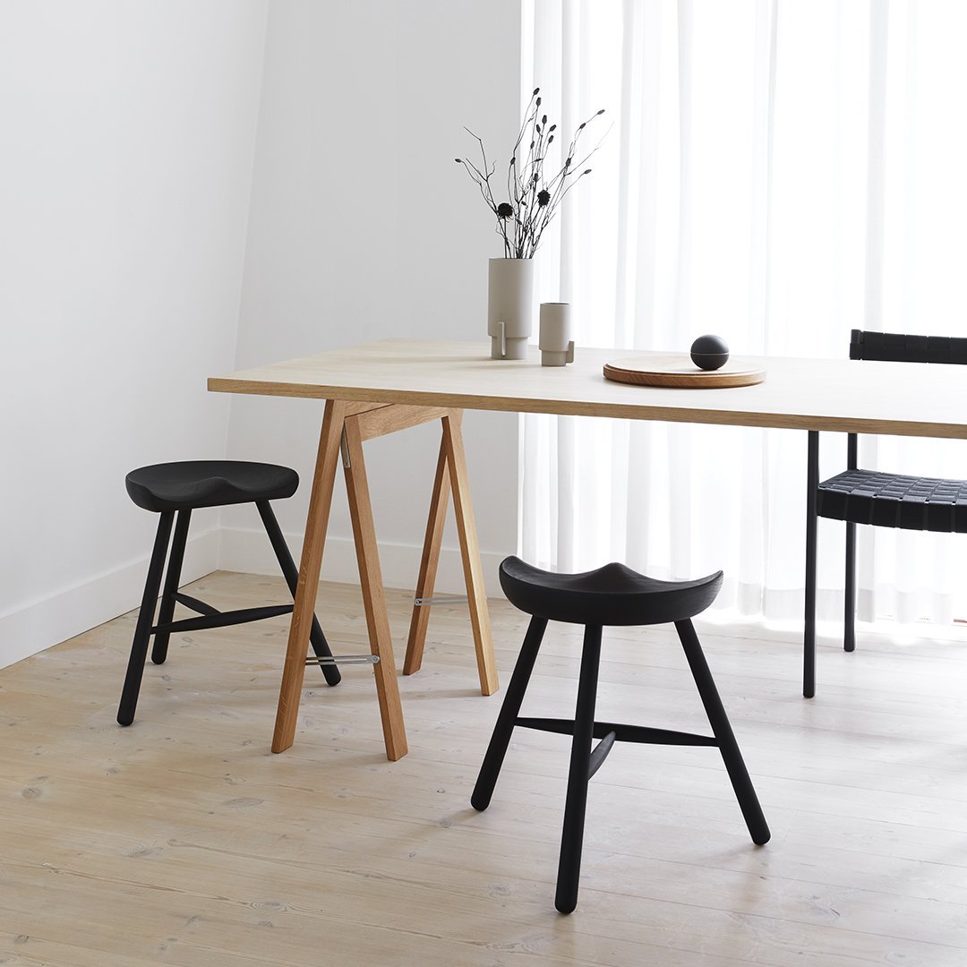 Modern wooden table with natural finish, paired with black stools and minimalist decor against a bright, airy backdrop.