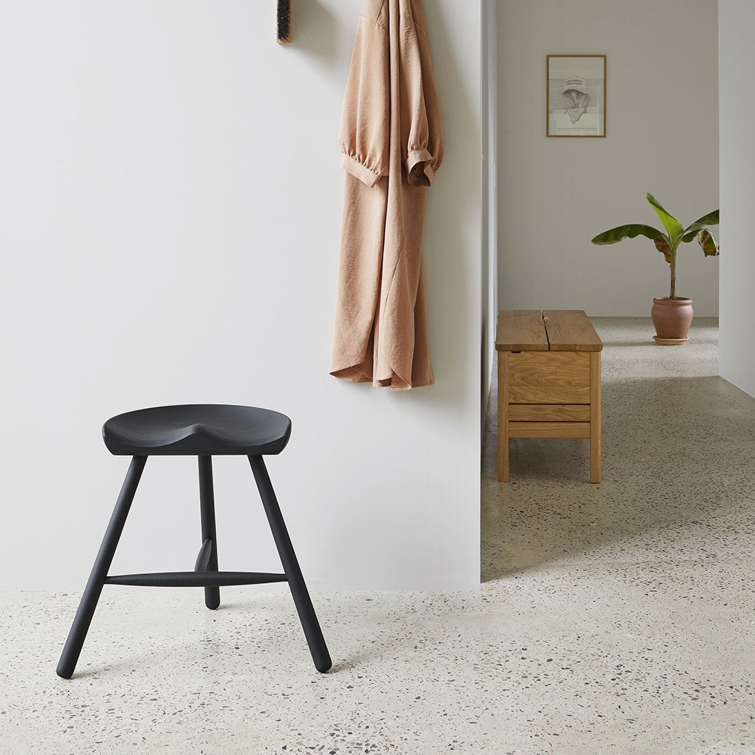 Black wooden stool against a neutral wall, featuring a seamless design and a minimalist aesthetic in soft earthy tones.