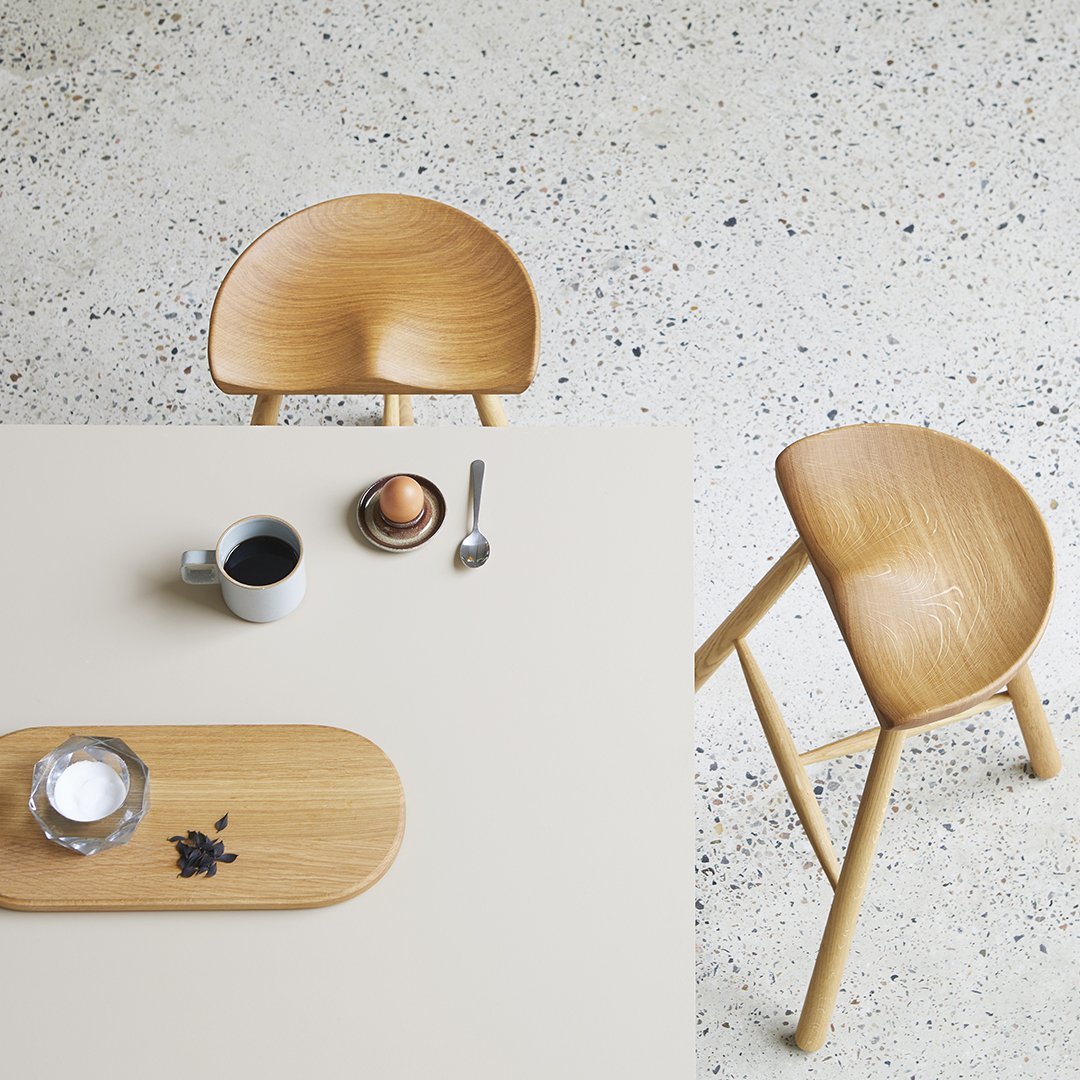 Light wood chair with a curved seat, neutral tabletop, and textured surface, featuring subtle speckled patterns.