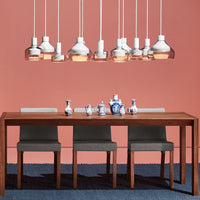 Delicate white and glass pendant lights hang above a warm wooden table, complemented by gray chairs on a blue textured rug.