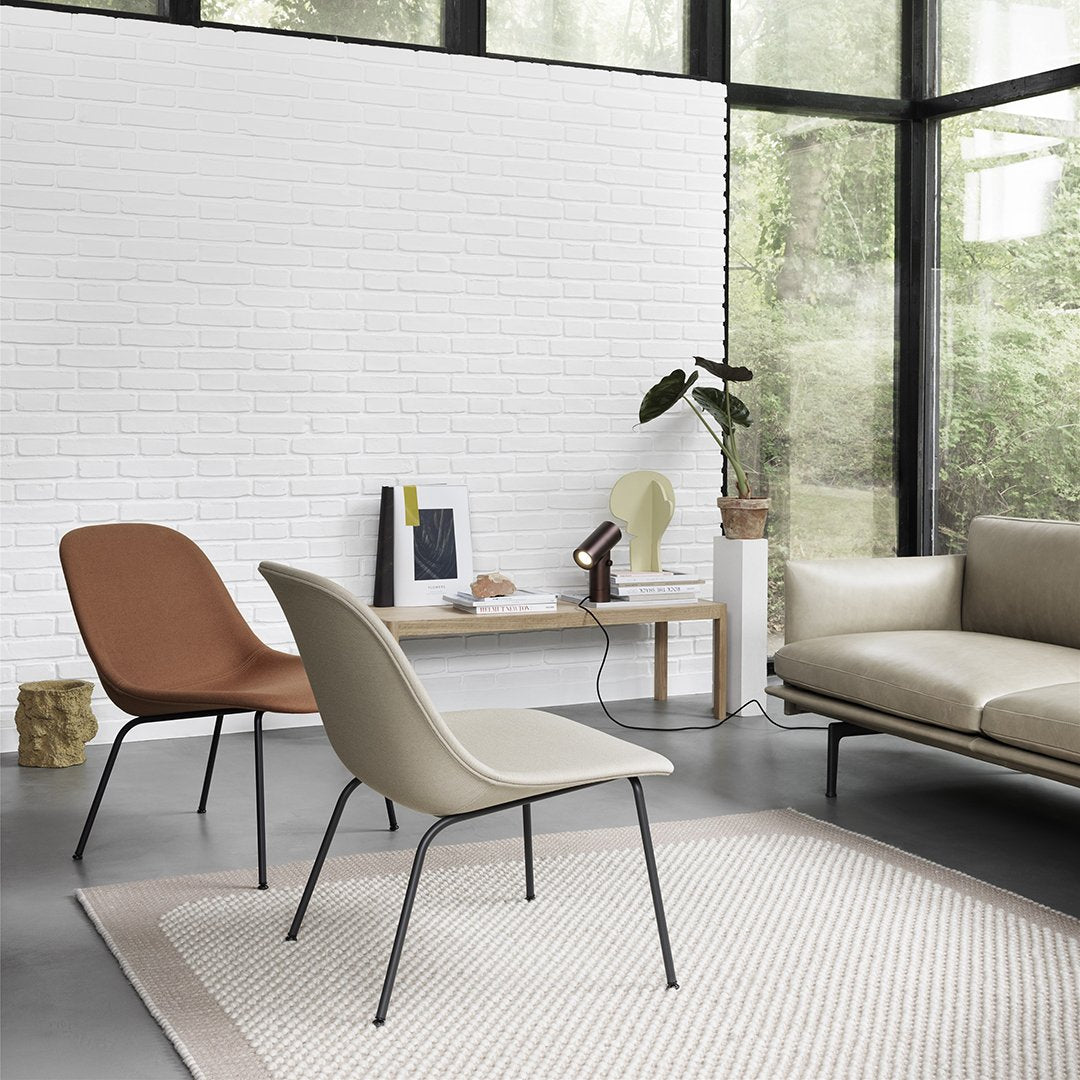 Modern chairs in warm tan and soft beige, set on a textured rug with a geometric pattern, against a white brick wall.