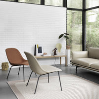 Modern chairs in warm tan and soft beige, set on a textured rug with a geometric pattern, against a white brick wall.