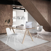 Modern wooden dining table with white chairs, light gray rug, and warm wood accents in a chic, minimalistic interior.