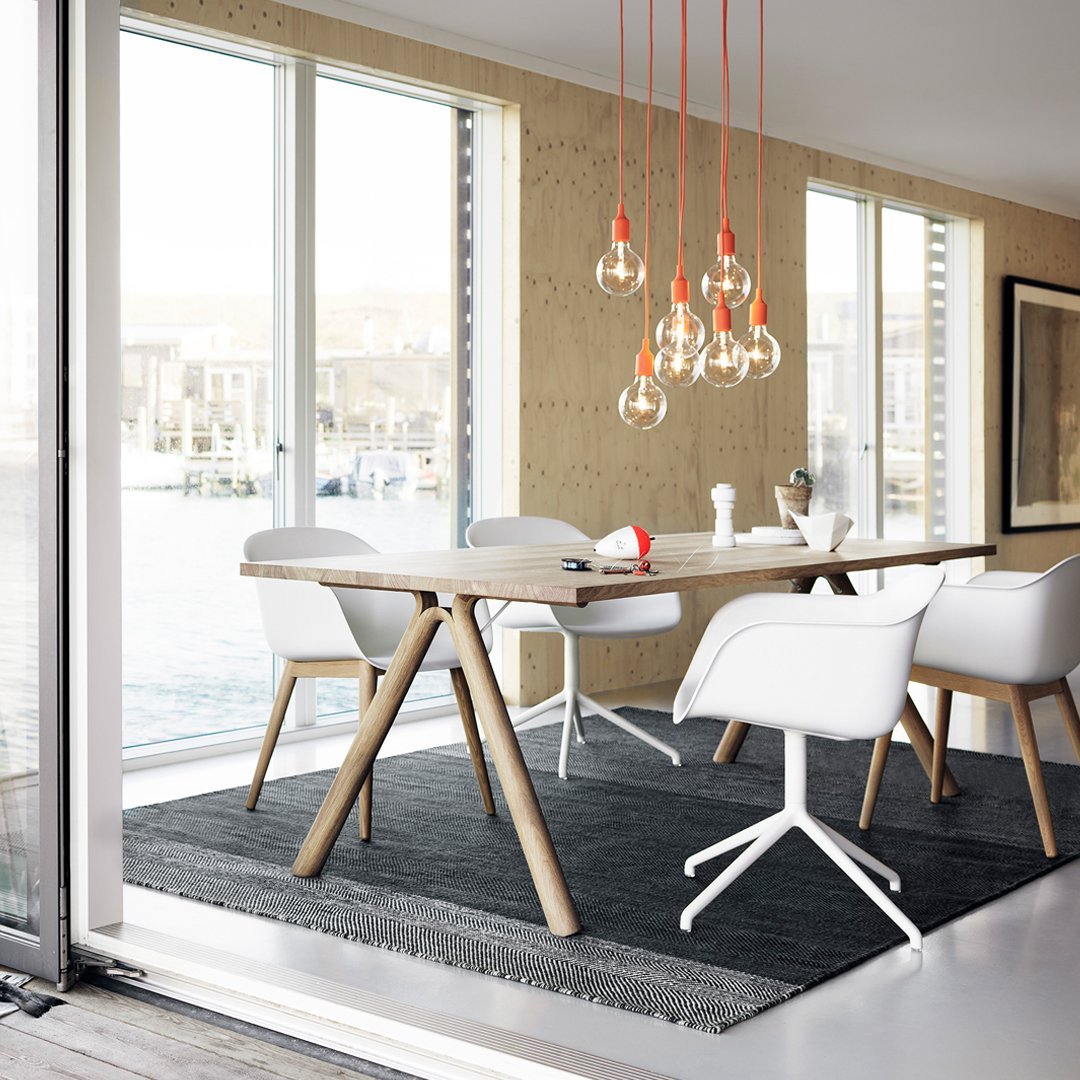 Modern dining room featuring a gray rug, white chairs, wooden table, and warm orange pendant lights. Stylish, minimalistic design.