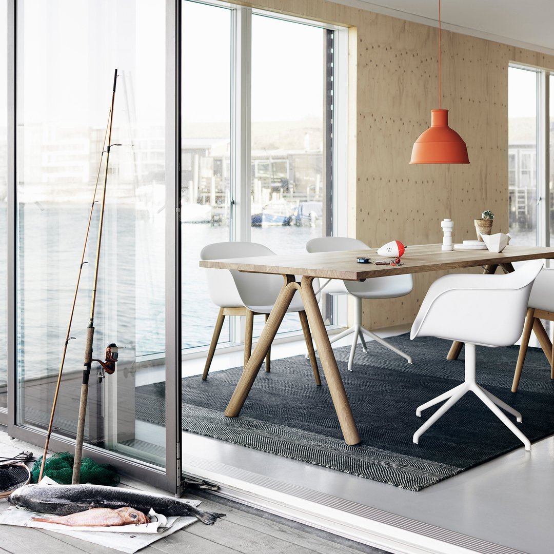 Modern dining room with white chairs, a wooden table, gray rug, and an orange pendant light. Bright, clean colors and patterns.