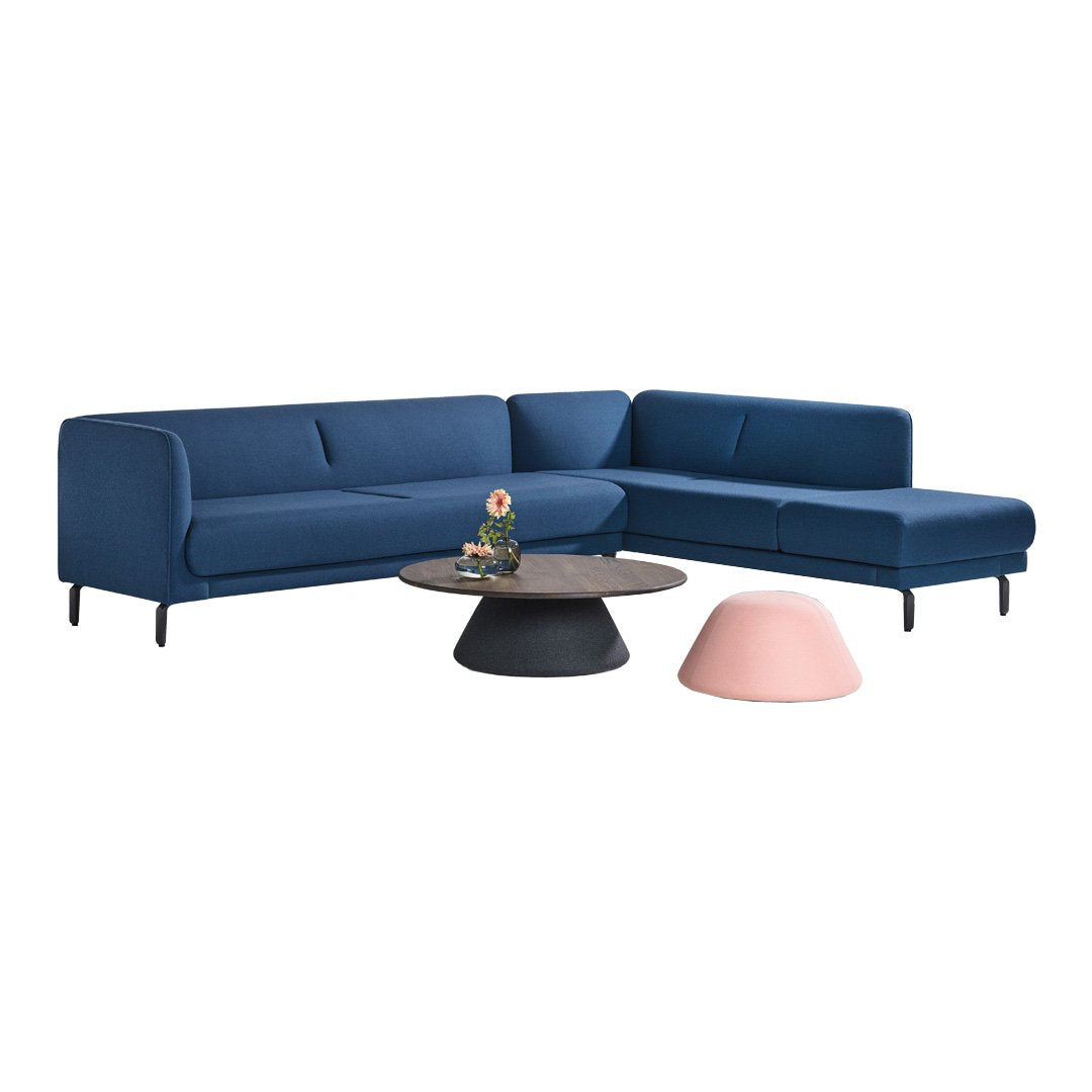 Blue sectional sofa with subtle texture, complemented by a round black coffee table and a soft pink accent piece.