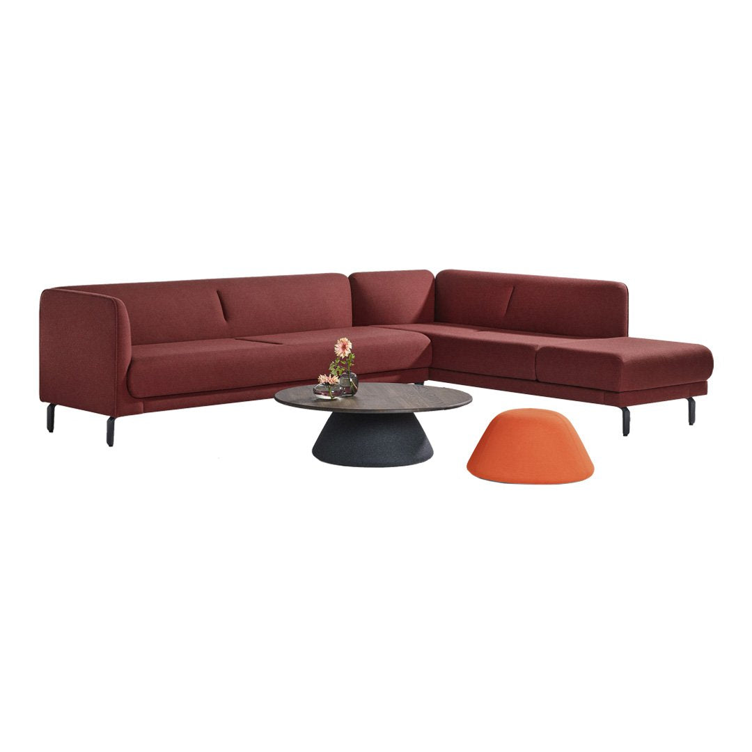 Modern burgundy sectional sofa with smooth fabric, complemented by a round black coffee table and bright orange accent piece.
