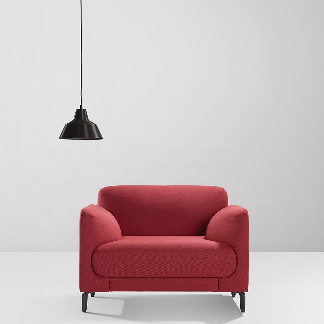 Red upholstered armchair with a smooth, minimalist design against a clean, neutral backdrop and black pendant light.