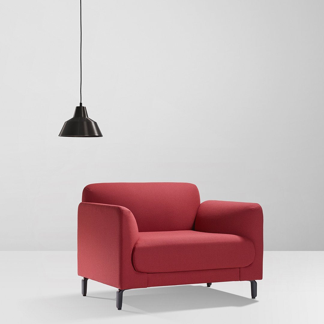 Red upholstered armchair with a smooth finish, paired with a sleek black pendant lamp. Modern minimalistic design.