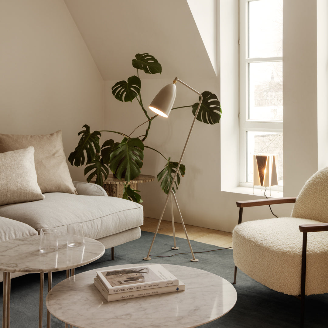 Minimalist living room featuring beige furniture, green plant accents, and geometric marble tables on a soft blue rug.