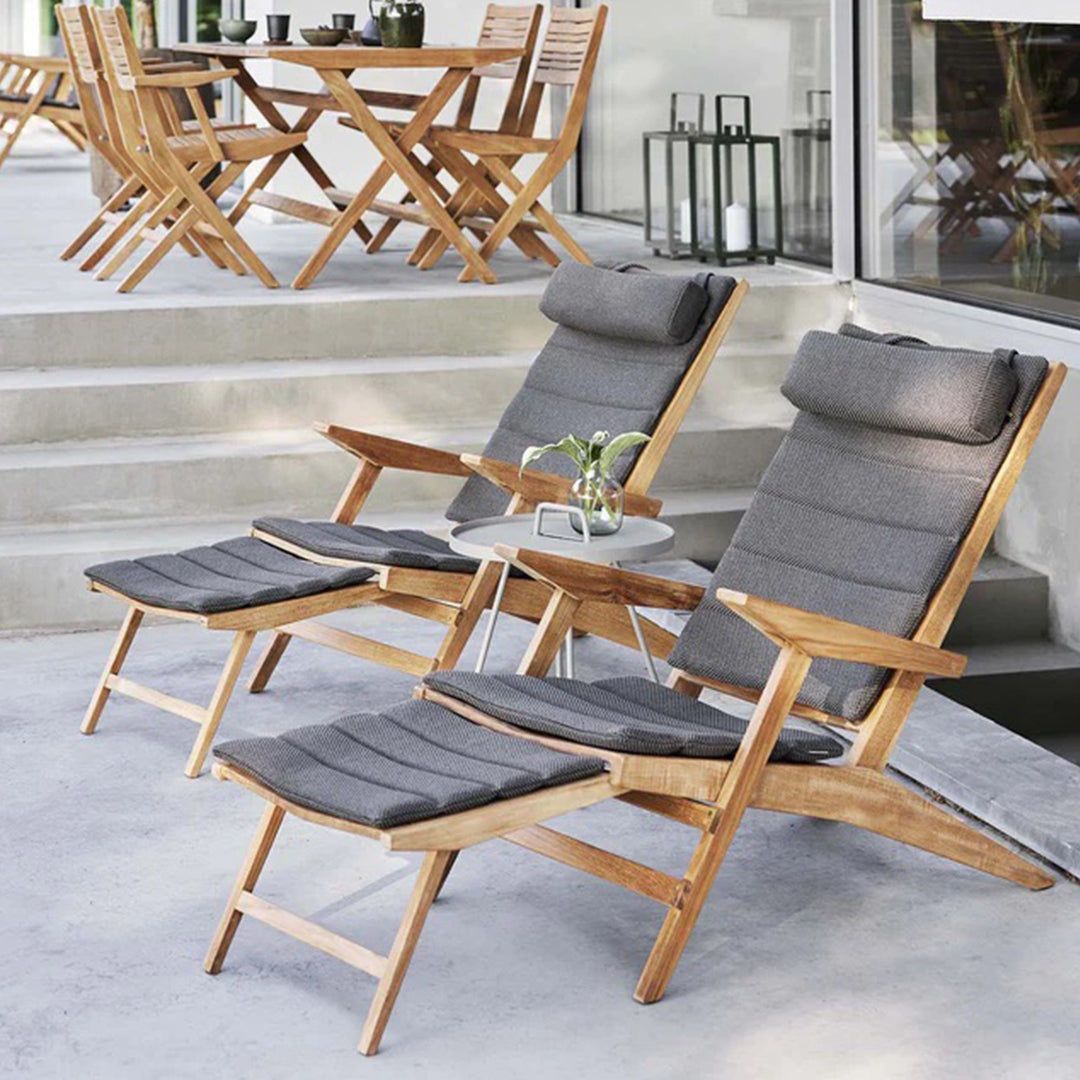 "Gray cushioned reclining chairs with wooden frames, set against a neutral outdoor backdrop."