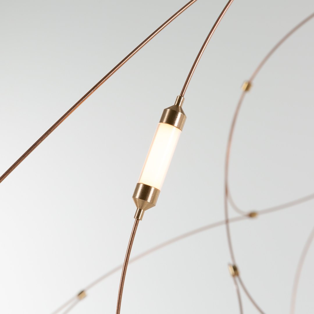 Modern pendant light with warm white and metallic gold accents on curved bronze wires against a sleek white background.