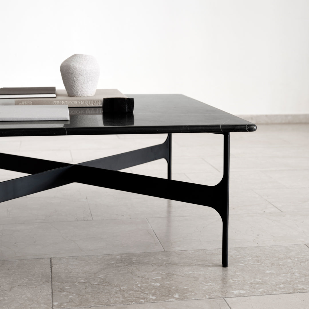 Sleek black coffee table with a minimalist design and smooth glass top, featuring cross-legged base.