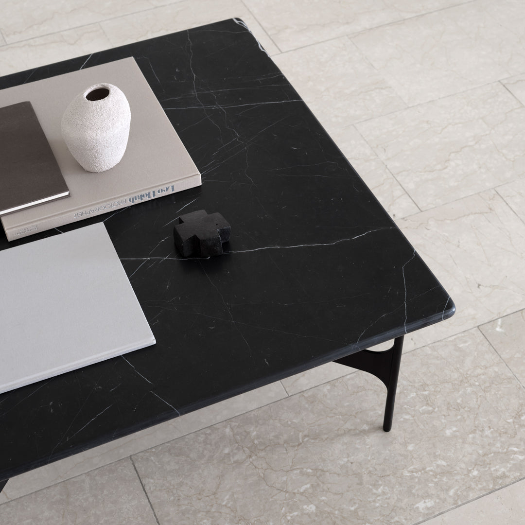 Black marble coffee table with white veining, paired with gray and matte accessories on a light stone floor.