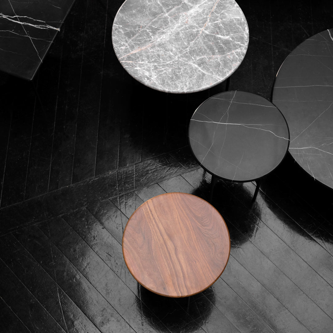 Round coffee tables in black, white marble, and rich wood tones with sleek, modern patterns on a glossy black floor.
