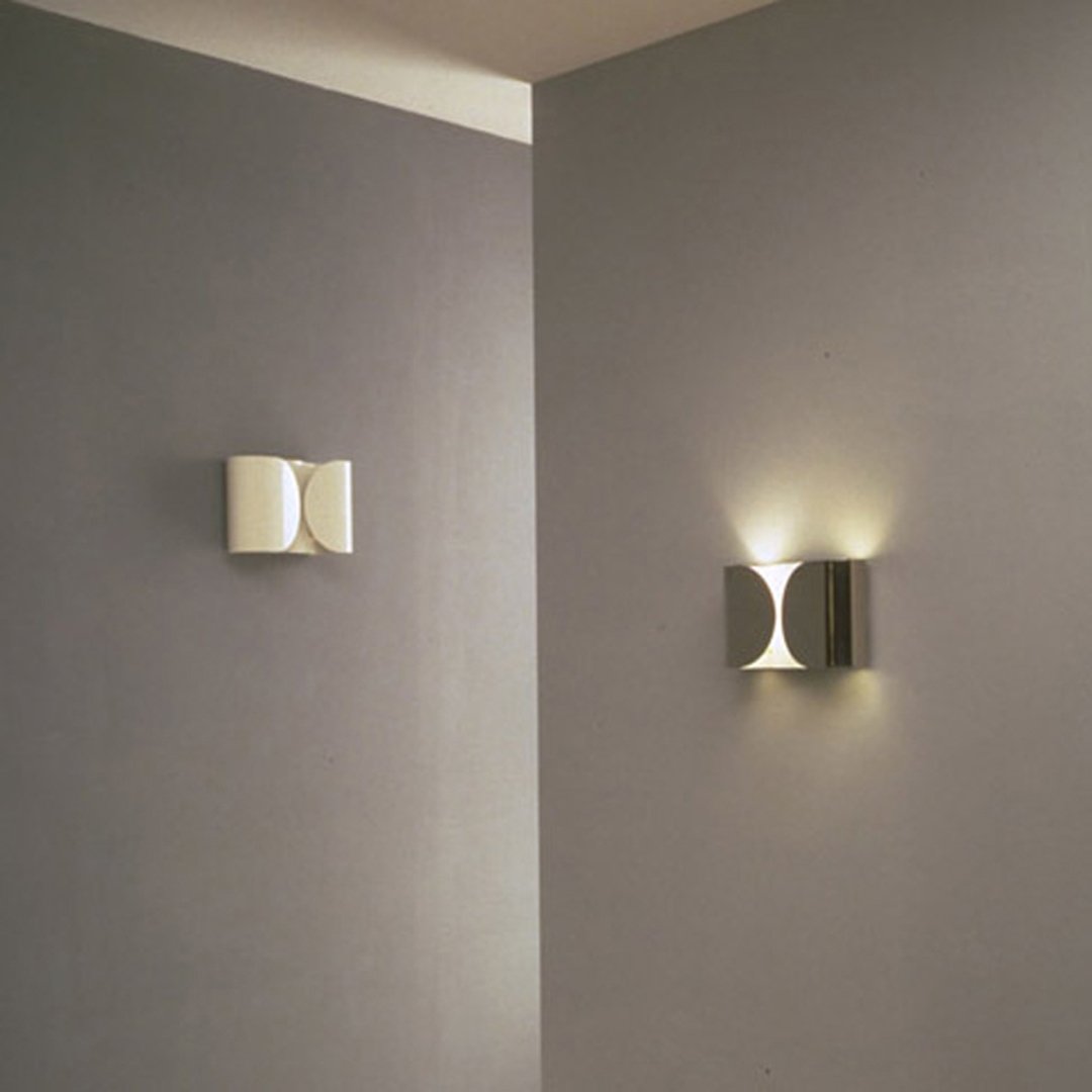 White and silver wall sconces with sleek, modern designs, casting soft light against gray walls.