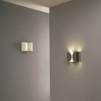 White and silver wall sconces with sleek, modern designs, casting soft light against gray walls.