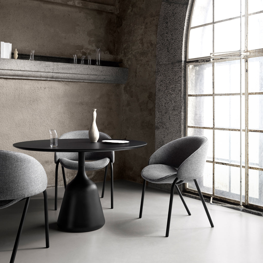 Modern black table with gray upholstered chairs, set against a minimalist industrial backdrop with soft natural light.