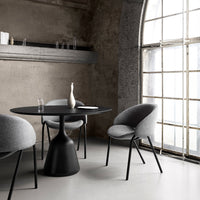 Modern black table with gray upholstered chairs, set against a minimalist industrial backdrop with soft natural light.