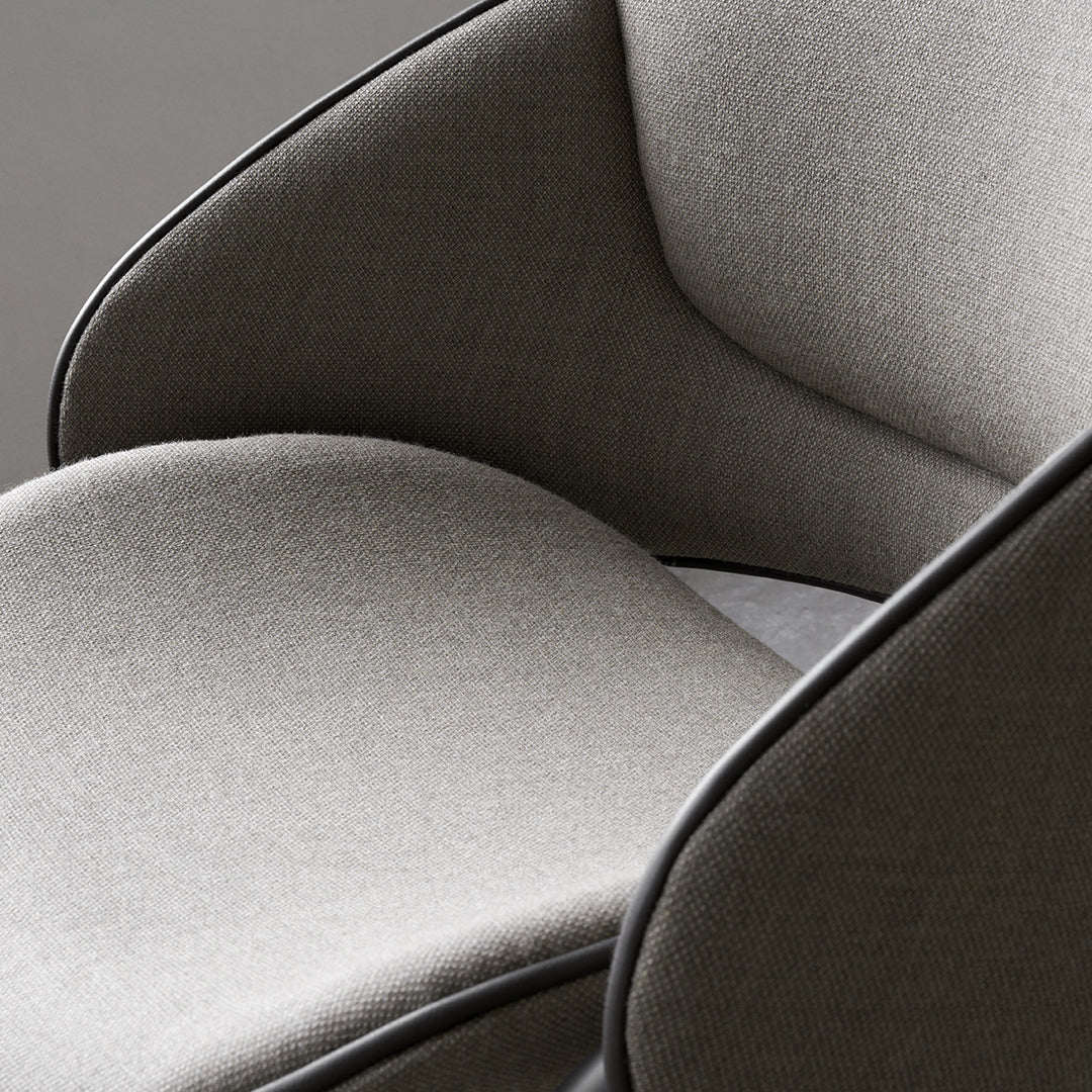 Grey upholstered chair with smooth, modern lines and contrasting black piping detail. Soft texture and minimalist style.