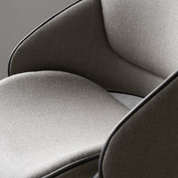 Grey upholstered chair with smooth, modern lines and contrasting black piping detail. Soft texture and minimalist style.