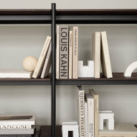 "Neutral-toned books with subtle textures on dark wooden shelves, accented by minimalist decor."