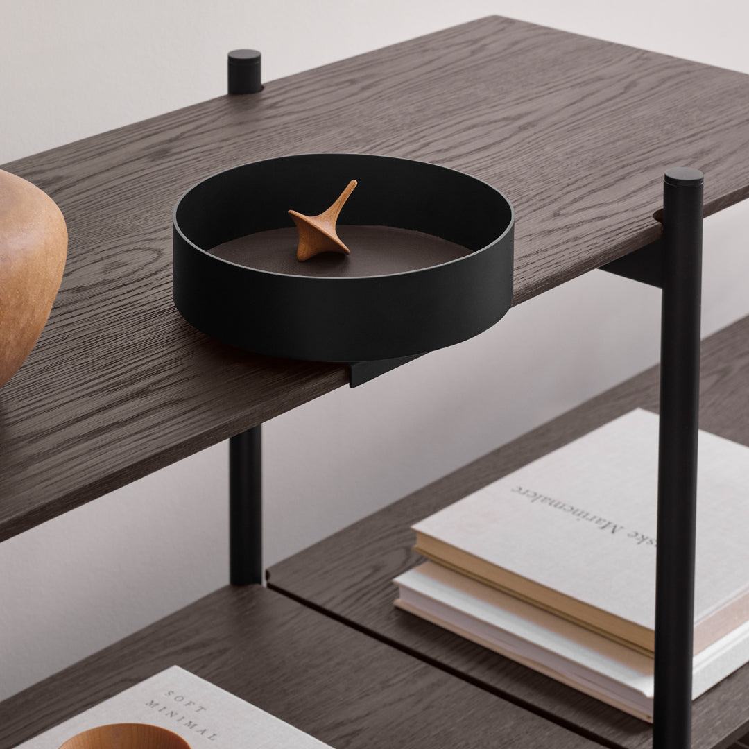 Black round tray on a dark wood shelf with minimalist design, featuring subtle earthy tones and clean lines.