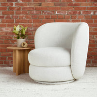 Textured off-white swivel chair against a red brick wall, with soft, rounded curves and a cozy appearance.
