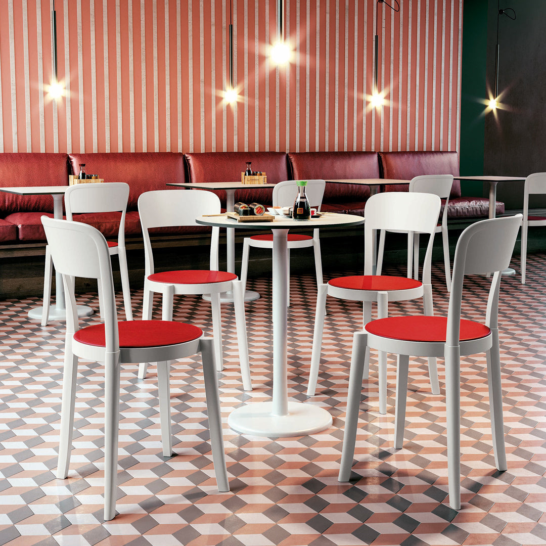 White dining chairs with red cushions set against a patterned tile floor and striped wall decor.