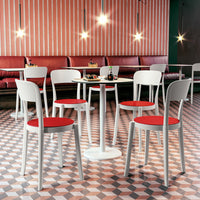 White chairs with red seats around a round table, set against pink and white geometric patterned flooring.