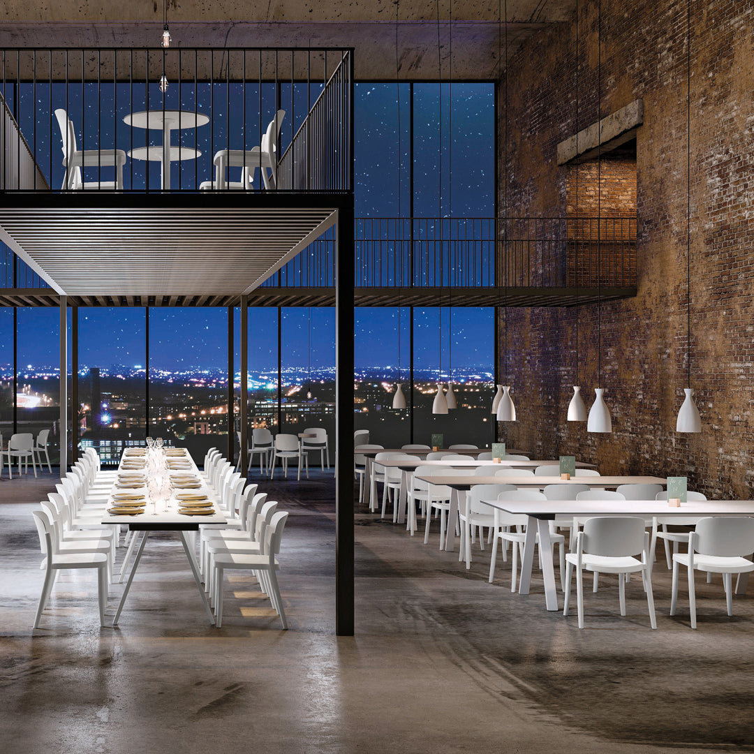 Modern dining space featuring sleek white furniture against a textured brick backdrop and large windows.