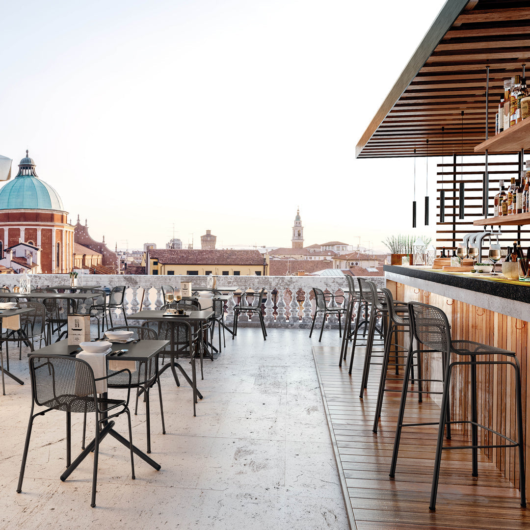 Black metal chairs and bar stools with wooden accents, set against a light, airy rooftop backdrop.