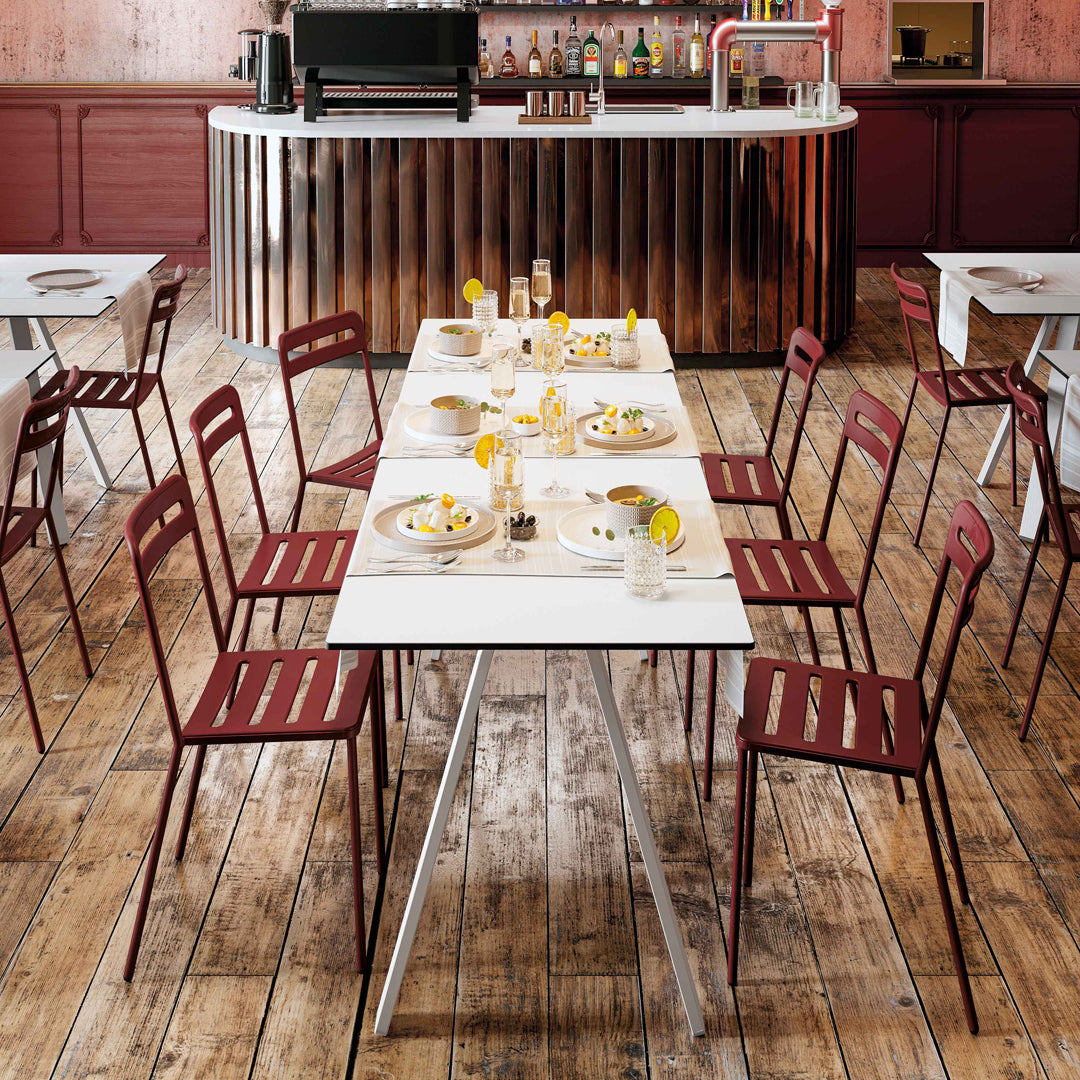 Red slatted chairs around a white table, set on a wooden floor in a stylish bar setting.