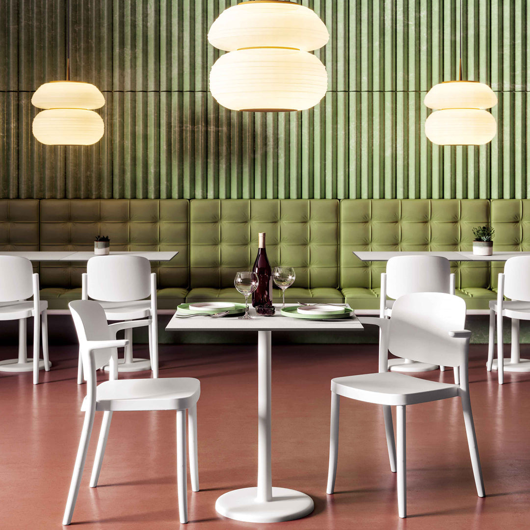 Modern white chairs and table set against a green paneled wall, with round pendant lights creating a warm ambiance.