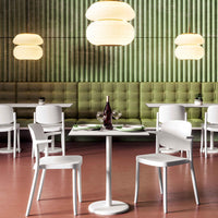 Modern white chairs and table set against a green paneled wall, with round pendant lights creating a warm ambiance.