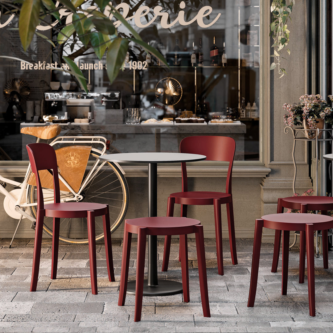 Red dining chairs and stools with a modern design, set against a stone-patterned floor and café backdrop.