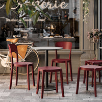 Red dining chairs and stools with a modern design, set against a stone-patterned floor and café backdrop.