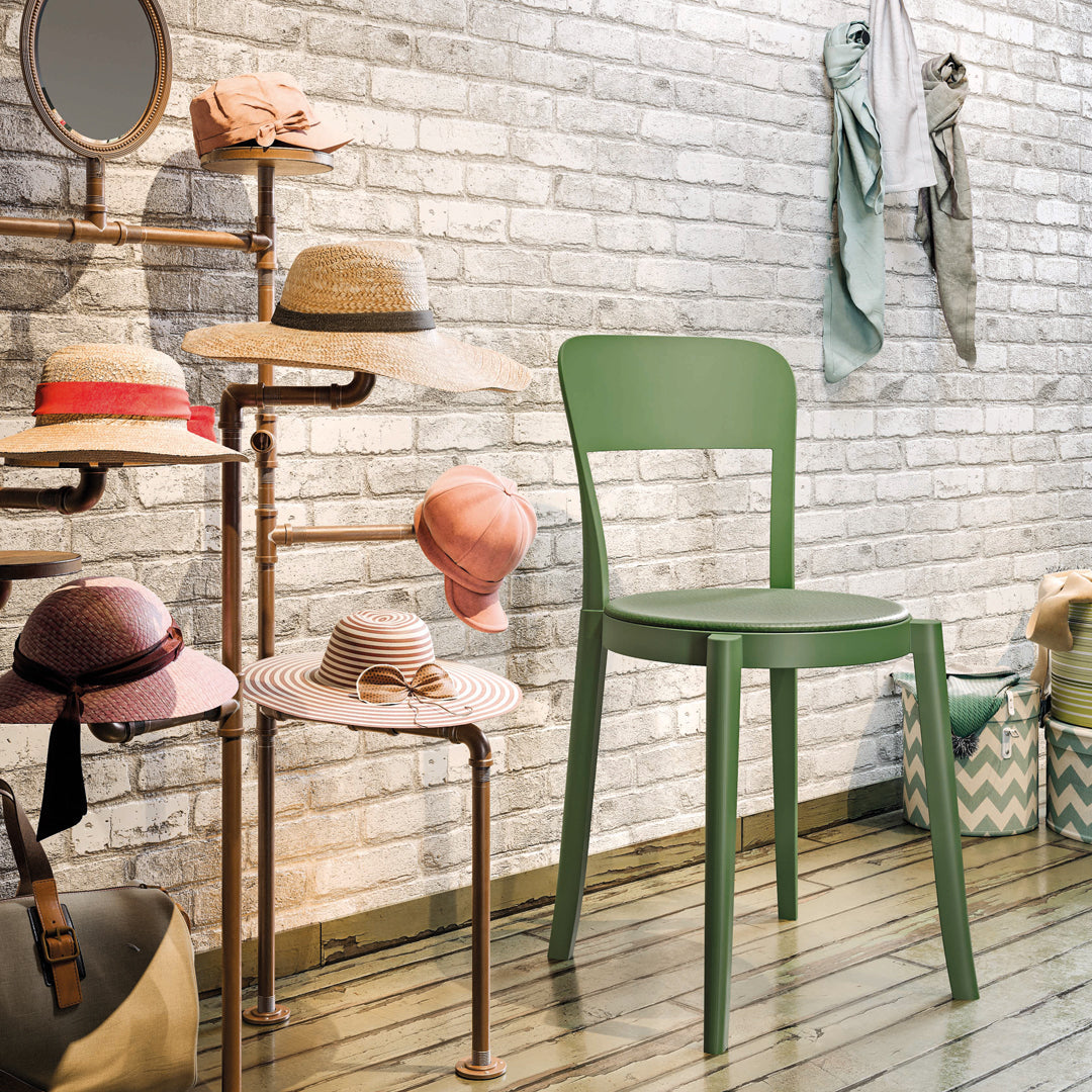 Green chair with a variety of pink and beige hats displayed against a textured white brick wall.